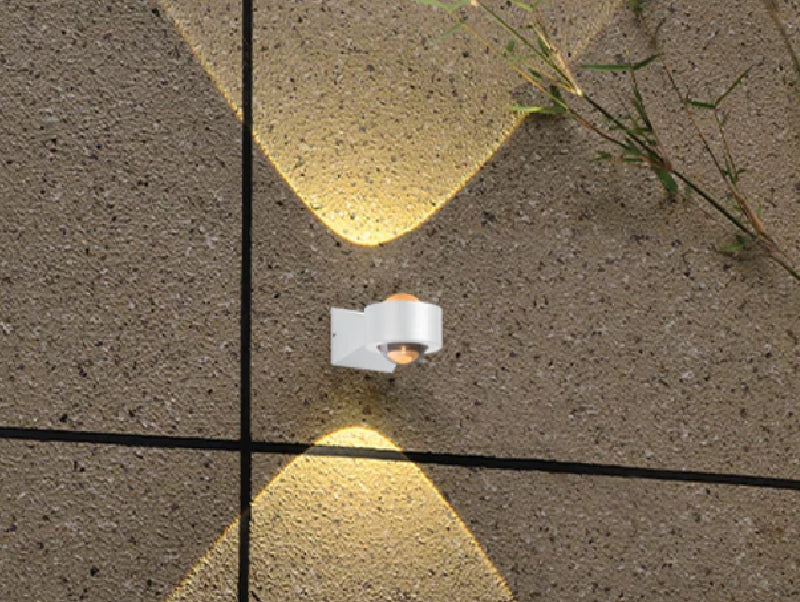 גוף תאורה לבן מותקן על קיר אבן ומפיץ אלומות אור כלפי מעלה ומטה