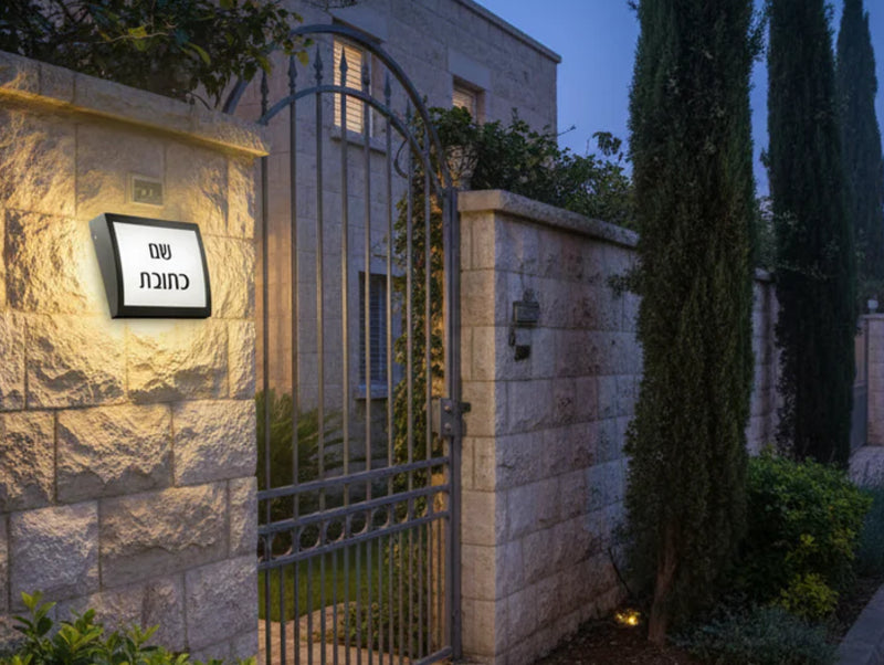 גוף תאורה צמוד קיר להארת שם וכתובת מותקן על קיר חיצוני ליד שער וכניסה לבית בשעת ערב.