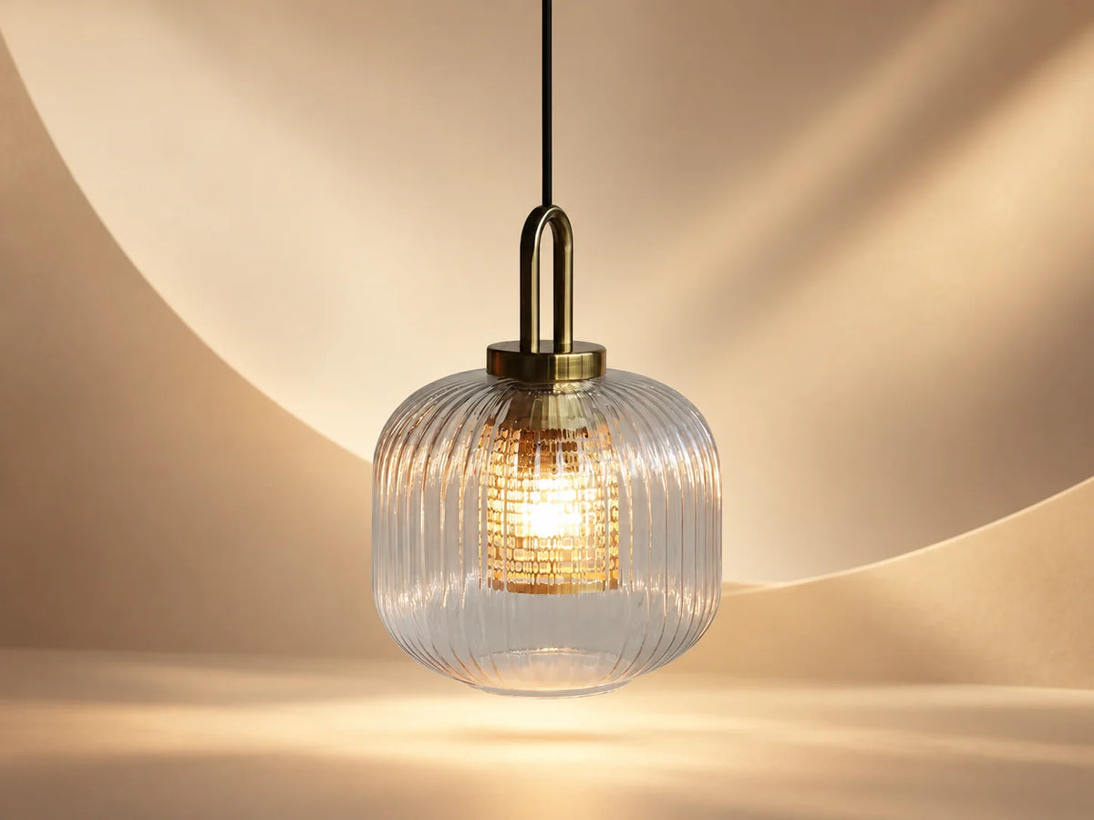 מנורת תליה LUZ תלויה מהתקרה, בעלת אהיל זכוכית שקופה עם חריצים עדינים וגימור פליז בחלקה העליון.