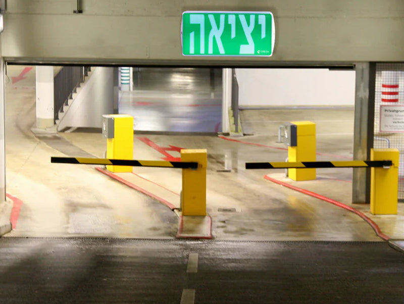 שלט יציאה ירוק מותקן מעל מעבר חניה עם מחסומי כניסה
