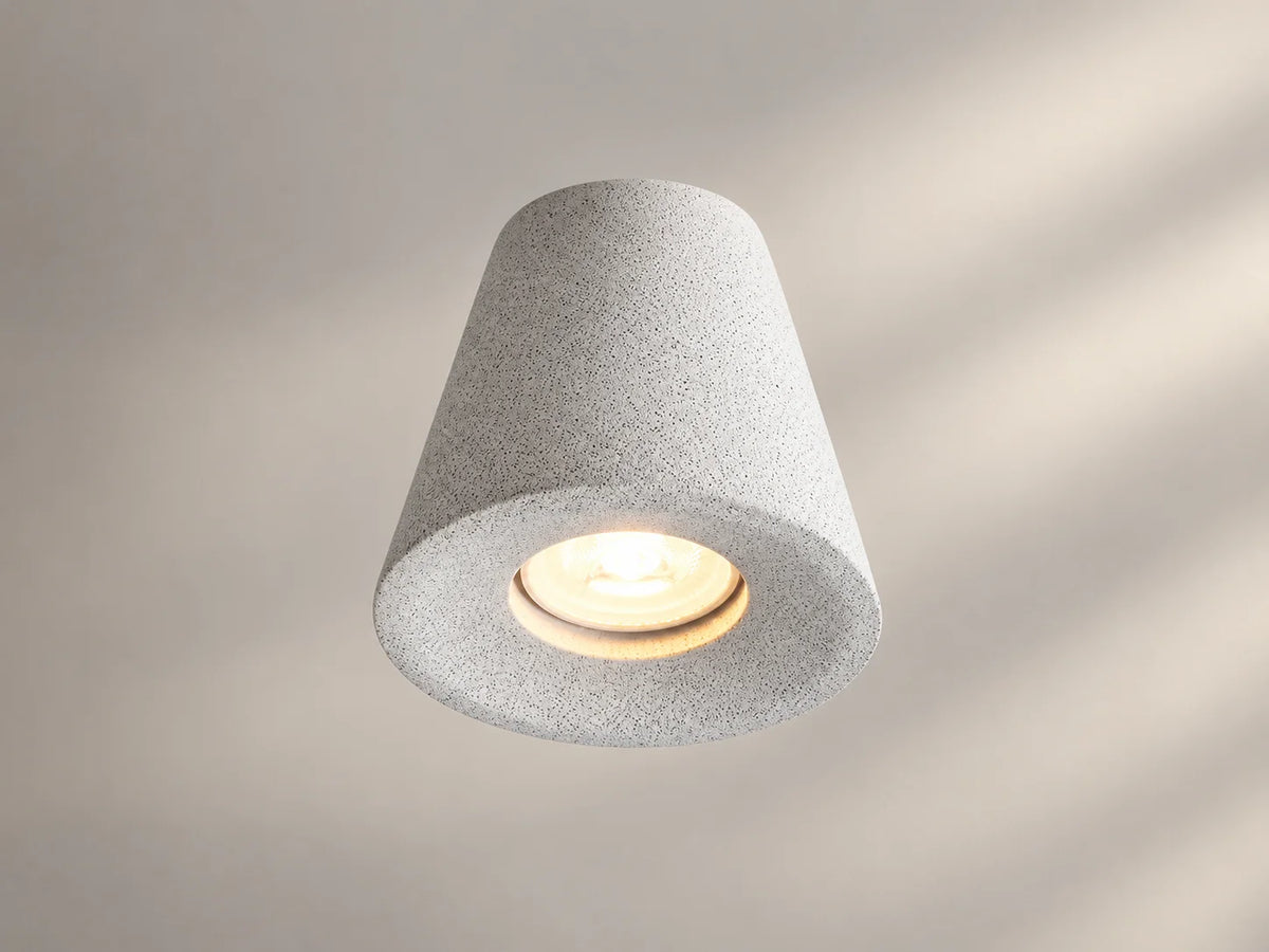 גוף תאורה צמוד תקרה ALTO של OMEGA, בצורת צילינדר מתרחב מטה, בגימור בטון בהיר עם נורה מוארת.